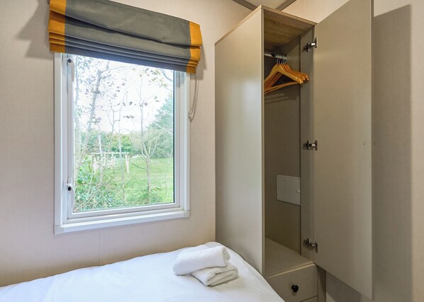 A bedroom with a bed, a window with a view of greenery, and a wardrobe with hanging space.