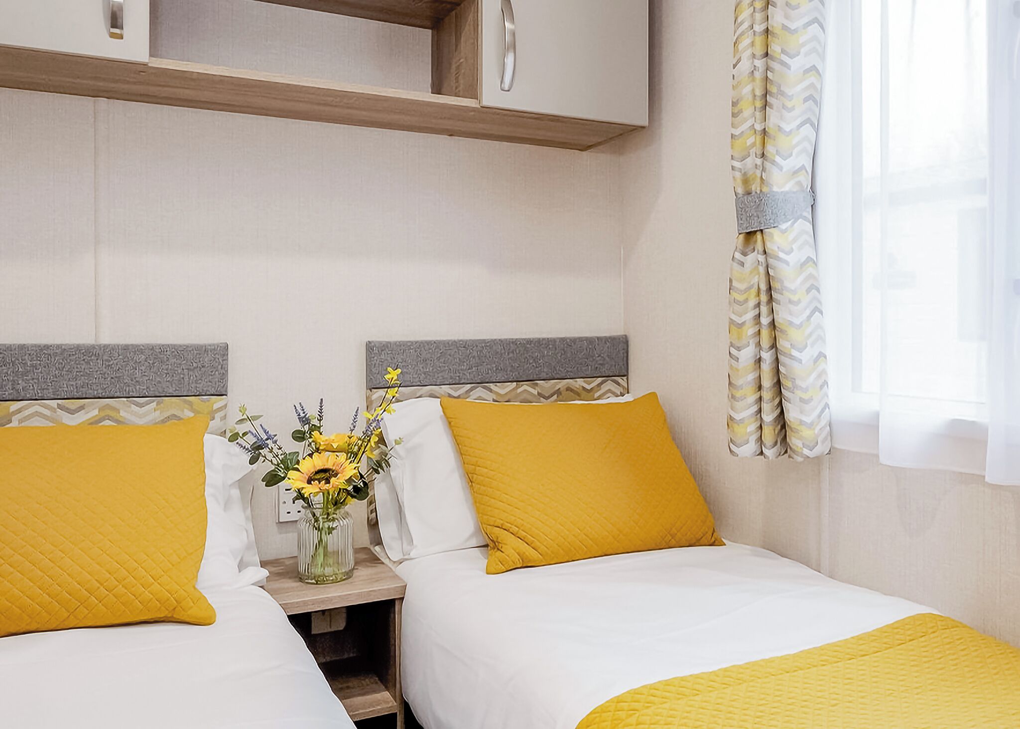 Une chambre d’hôtel avec deux lits, une table de chevet ornée d’un vase de fleurs et une fenêtre avec des rideaux.