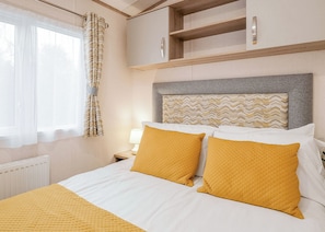 A hotel room with a bed, a nightstand, a lamp, a window with curtains, and a headboard with a patterned design. - Superior 3 Bed (Pet) (Hayle)