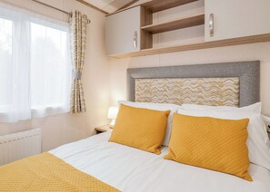 Une chambre d’hôtel comprenant un lit, une table de chevet, une lampe, une fenêtre avec des rideaux et une tête de lit ornée d’un motif.