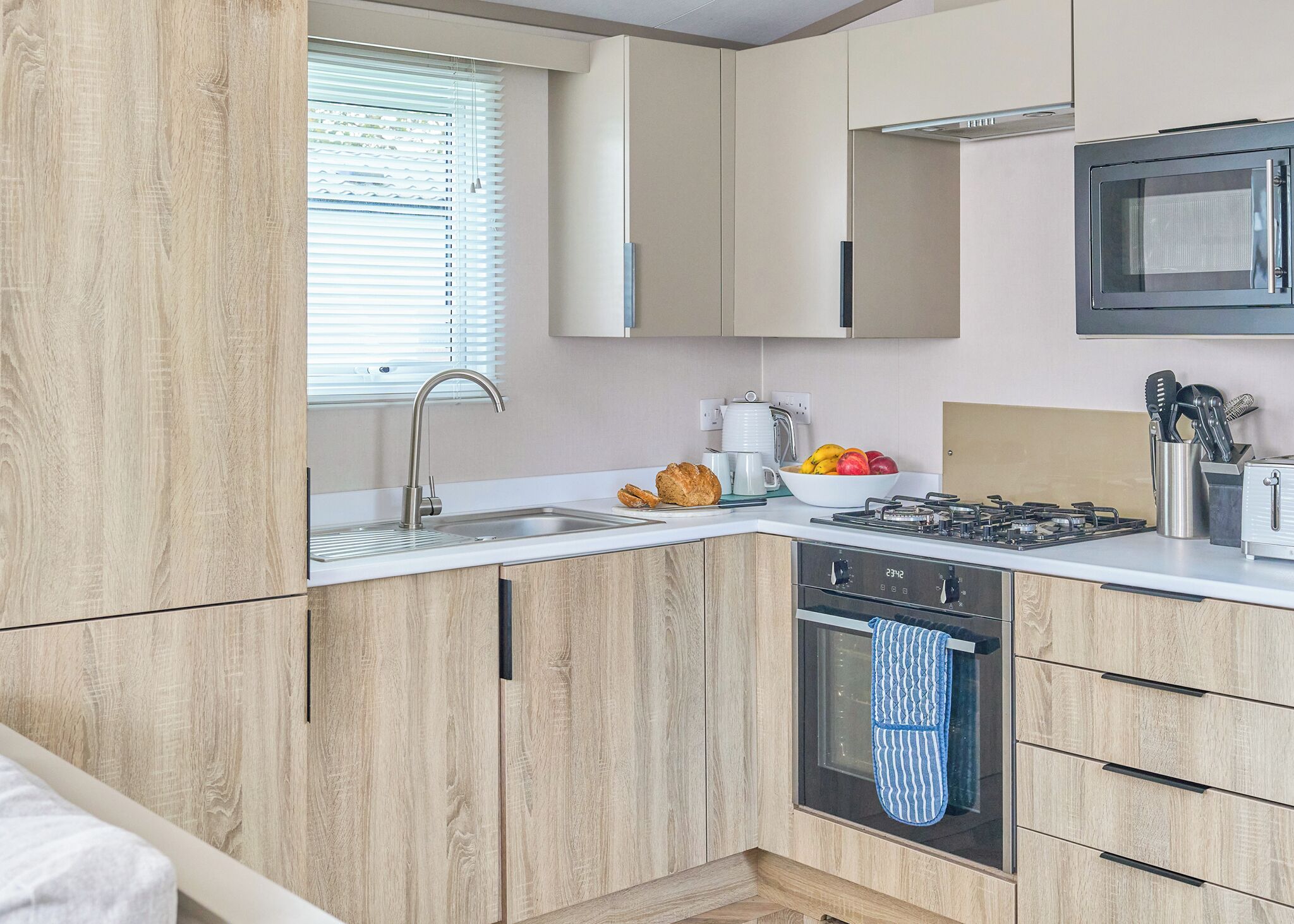 A modern kitchen with a built-in oven, a sink, and a window with blinds.