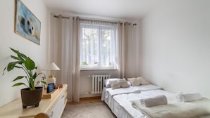 Een hotelkamer met een bed, een bureau met lamp, een kamerplant en een raam met gordijnen.