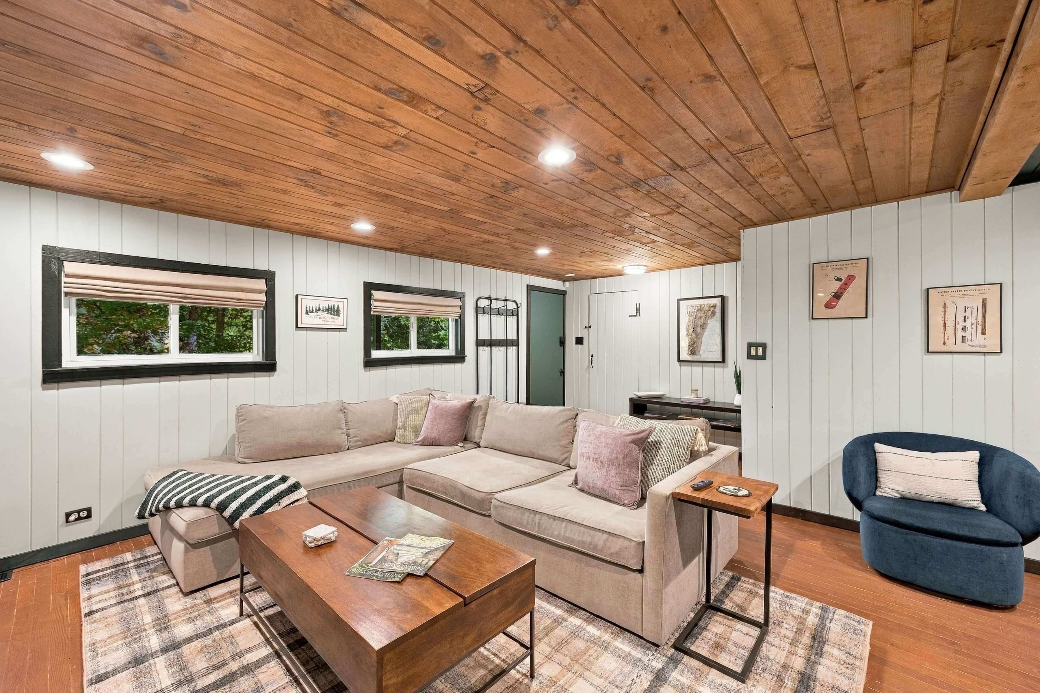 Un salon chaleureux avec un plafond en bois, un canapé d’angle beige, un fauteuil bleu et une table basse en bois.