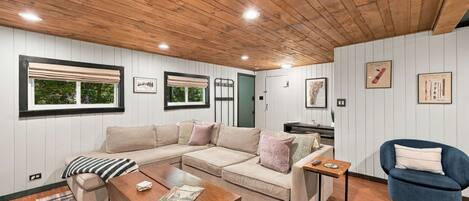 Un salon chaleureux avec un plafond en bois, un canapé d’angle beige, un fauteuil bleu et une table basse en bois.