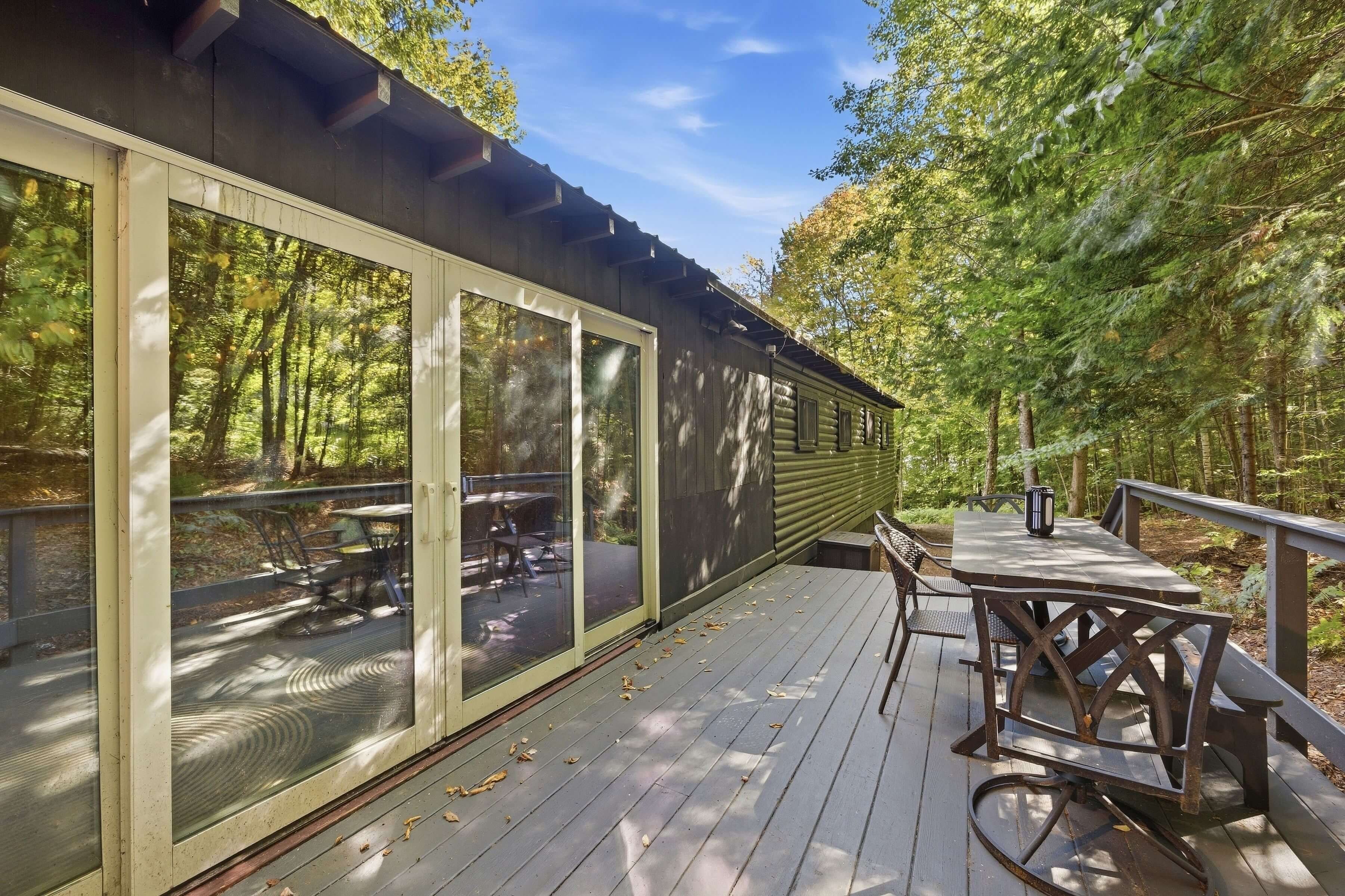 A wooden deck with a table and chairs, surrounded by a forest.