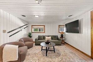 A living room with a sofa, armchairs, a coffee table, a TV, and skis on the wall. - Cabin Near Stratton and Mt. Snow w/hot tub, sauna (Wardsboro)