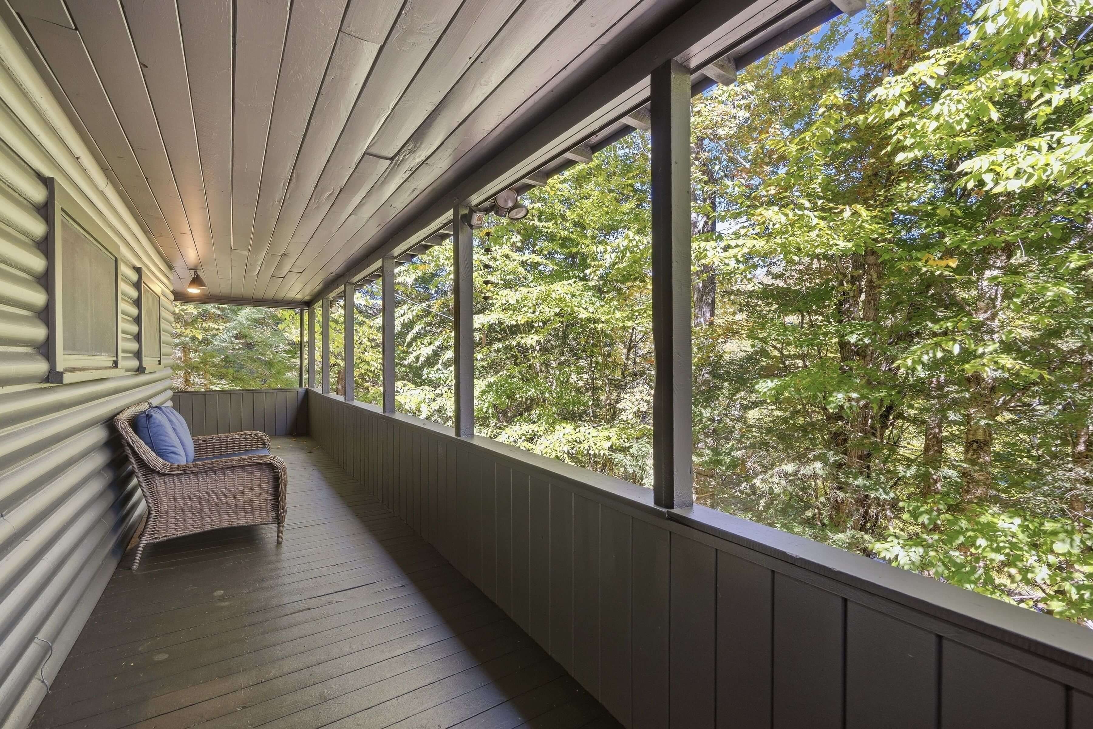 A covered porch with a wicker chair and a view of a forest.