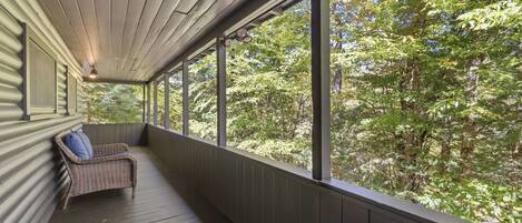 A covered porch with a wicker chair and a view of a forest.