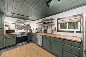 Een keuken met groene kastjes, roestvrijstalen apparatuur en een houten aanrecht.