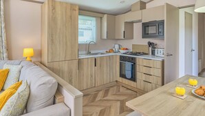 A compact kitchen with wooden cabinets, a microwave, and a gas stove. - Superior 3 Bedroom sleeps 8 (Hayle)