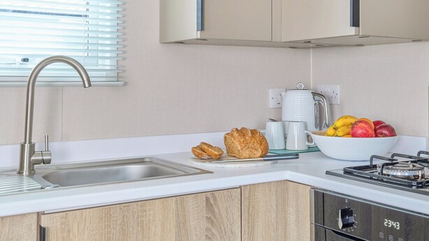 A modern kitchen with a stainless steel sink, wooden cabinets, a gas stove, and a bowl of fruit. - Superior 3 Bedroom sleeps 8 (Hayle)