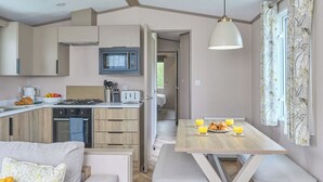 A compact kitchen with a microwave, toaster, and stove, a dining area with a table and bench, and a cozy seating area with a sofa.