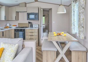 A compact kitchen with a microwave, toaster, and stove, a dining area with a table and bench, and a cozy seating area with a sofa. - Superior 3 Bedroom sleeps 8 (Hayle)