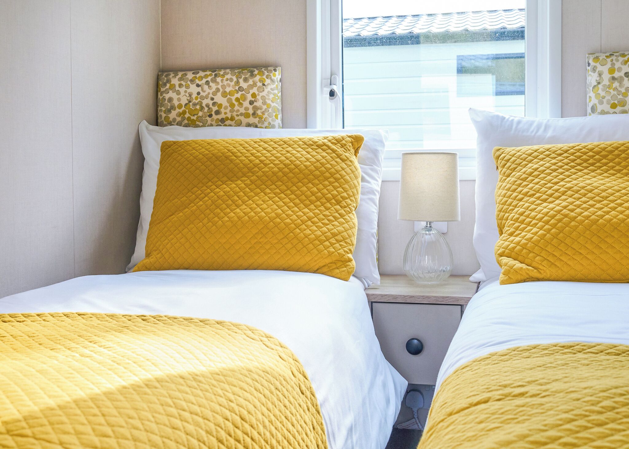 A hotel room with two beds, each with yellow bedding, a bedside lamp, and a window with a view of a building.