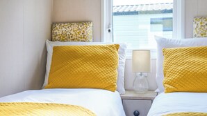 A hotel room with two beds, each with yellow bedding, a bedside lamp, and a window with a view of a building. - Superior 3 Bedroom sleeps 8 (Hayle)