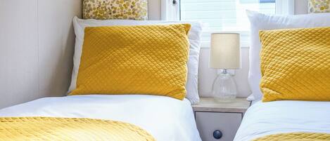 A hotel room with two beds, each with yellow bedding, a bedside lamp, and a window with a view of a building.