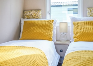 A hotel room with two beds, each with yellow bedding, a bedside lamp, and a window with a view of a building. - Superior 3 Bedroom sleeps 8 (Hayle)