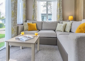 A modern living room with a grey sectional sofa, a small table with a magazine, two glasses of orange juice, and a lamp on a wooden side table. - Superior 3 Bedroom sleeps 8 (Hayle)