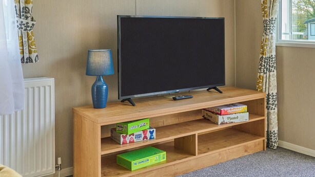 A living room with a television on a wooden stand, a lamp, and shelves with board games.
