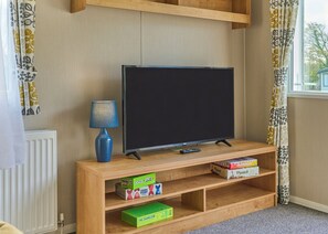 Een woonkamer met een televisie op een houten standaard, een lamp en planken met gezelschapsspellen.