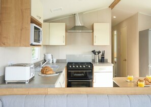 Een moderne keuken met een broodrooster, oven, spoelbak en een ontbijtgedeekte tafel met croissants en sinaasappelsap.