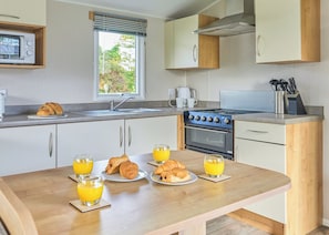 A modern kitchen with a dining table set for breakfast, including croissants and orange juice. - Superior 3 Bedroom sleeps 8 (Hayle)