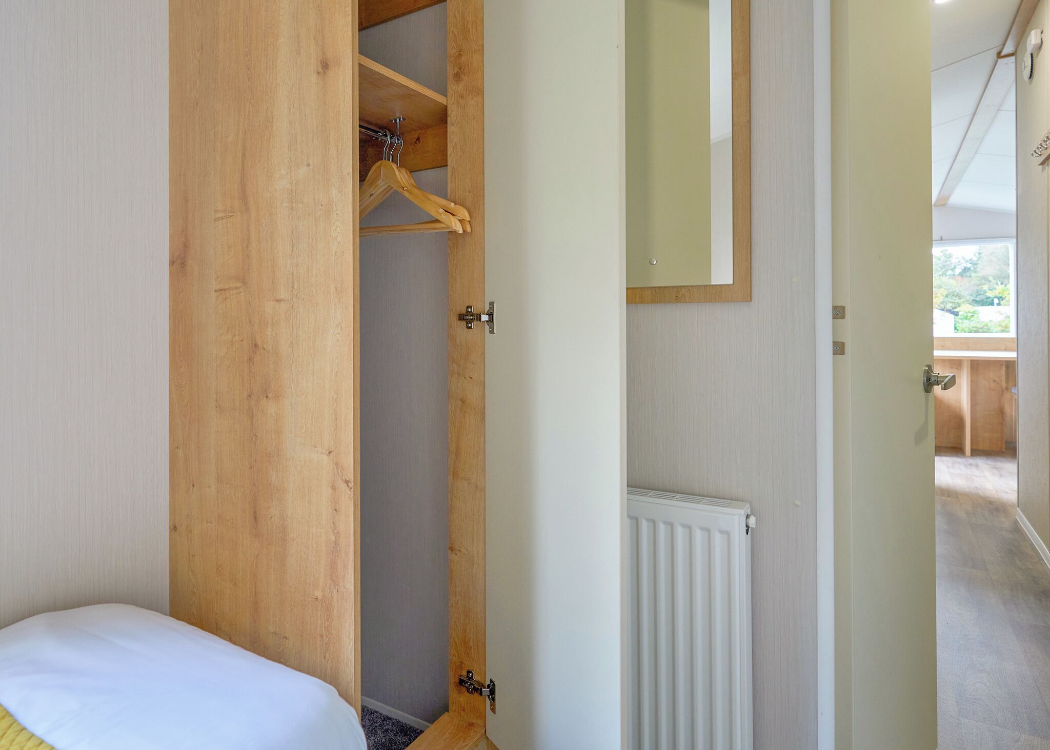 A bedroom with a wooden wardrobe, a bed, a radiator, and a mirror on the wall.