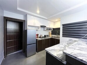 A compact kitchen with dark cabinets, a stainless steel refrigerator, a microwave, and a marble countertop. - Deluxe Indulgence Hotel and Suites (Abuja)
