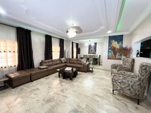 A living room with a sectional sofa, patterned armchair, and a coffee table. - Deluxe Indulgence Hotel and Suites (Abuja)