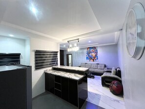 A modern kitchen with a marble countertop, a built-in oven, and a dining area with a sofa and a rug. - Deluxe Indulgence Hotel and Suites (Abuja)