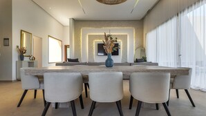 Ein moderner Essraum mit einem großen rechteckigen Tisch, sechs Stühlen und einer Vase mit getrockneten Blumen.