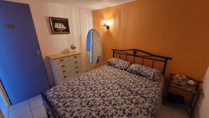 Un dormitorio con cama, cómoda, espejo y lámpara de pared.