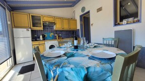 Un comedor con una mesa preparada para dos, una cocina con armarios amarillos y un ventanal con vistas.