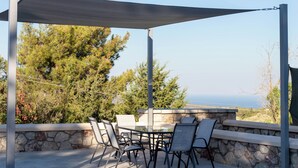 Um pátio externo com mesa e cadeiras, paredes de pedra e vista para o mar.