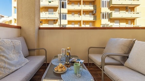 A balcony with a table set for two, a sofa, and a view of a yellow building with multiple balconies. - First-floor Apartment Just Steps From the sea (Alghero)