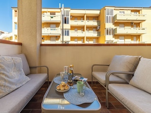 A balcony with a table set for two, a sofa, and a view of a yellow building with multiple balconies. - First-floor Apartment Just Steps From the sea (Alghero)