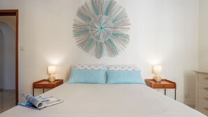 A bedroom with a bed, two bedside tables, a wall-mounted decorative piece, and a magazine on the bed. - First-floor Apartment Just Steps From the sea (Alghero)