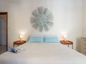 A bedroom with a bed, two bedside tables, a wall-mounted decorative piece, and a magazine on the bed. - First-floor Apartment Just Steps From the sea (Alghero)