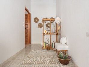A hallway with a patterned rug, a wooden door, a white chair, a small table with a potted plant, and a wooden shelf with decorative items. - First-floor Apartment Just Steps From the sea (Alghero)