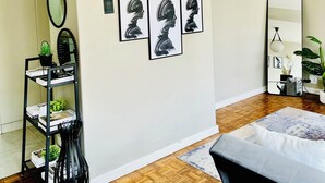 Een moderne slaapkamer met een houten vloer, een bed, een zwart-wit abstract schilderij, een spiegel en een zwart metalen plank met planten.