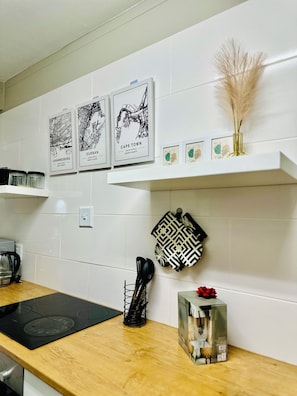 A kitchen with white tiles, a black induction cooktop, a coffee maker, and framed cityscape artwork on the wall. - Home Across The Sea🌊 (Humewood)