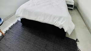 Een slaapkamer met een bed, een raam met zonwering, een nachtkastje met een lamp en een aan de muur hangend kunstwerk.