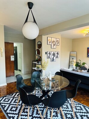 A modern dining area with a glass table, black chairs, and a patterned rug.