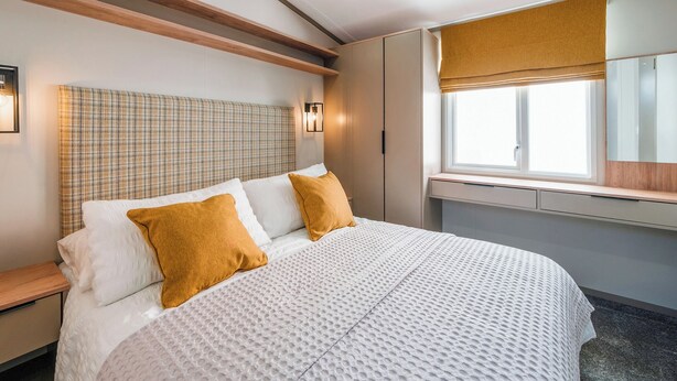 Habitación de hotel con cama, cabecera, mesitas de noche, ventana con vistas y lámpara fijada a la pared.