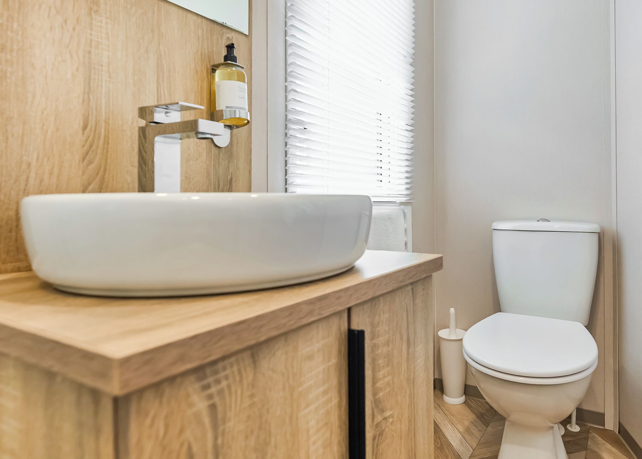 A bathroom with a wooden vanity, a white sink, a toilet, and a window with blinds.