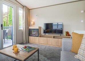 A living room with a TV, sofa, coffee table, and a view of the outdoors. - Luxury Holiday Home 3 bed (Hayle)