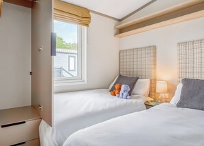A hotel room with two beds, a window with a view, a bedside table with a lamp, and a wardrobe. - Luxury Holiday Home 3 bed (Hayle)
