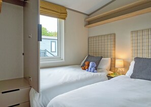 A hotel room with two beds, a window with a view, a bedside table with a lamp, and a wardrobe. - Luxury 3 bedroom Hot Tub sleeps 8 (Hayle)
