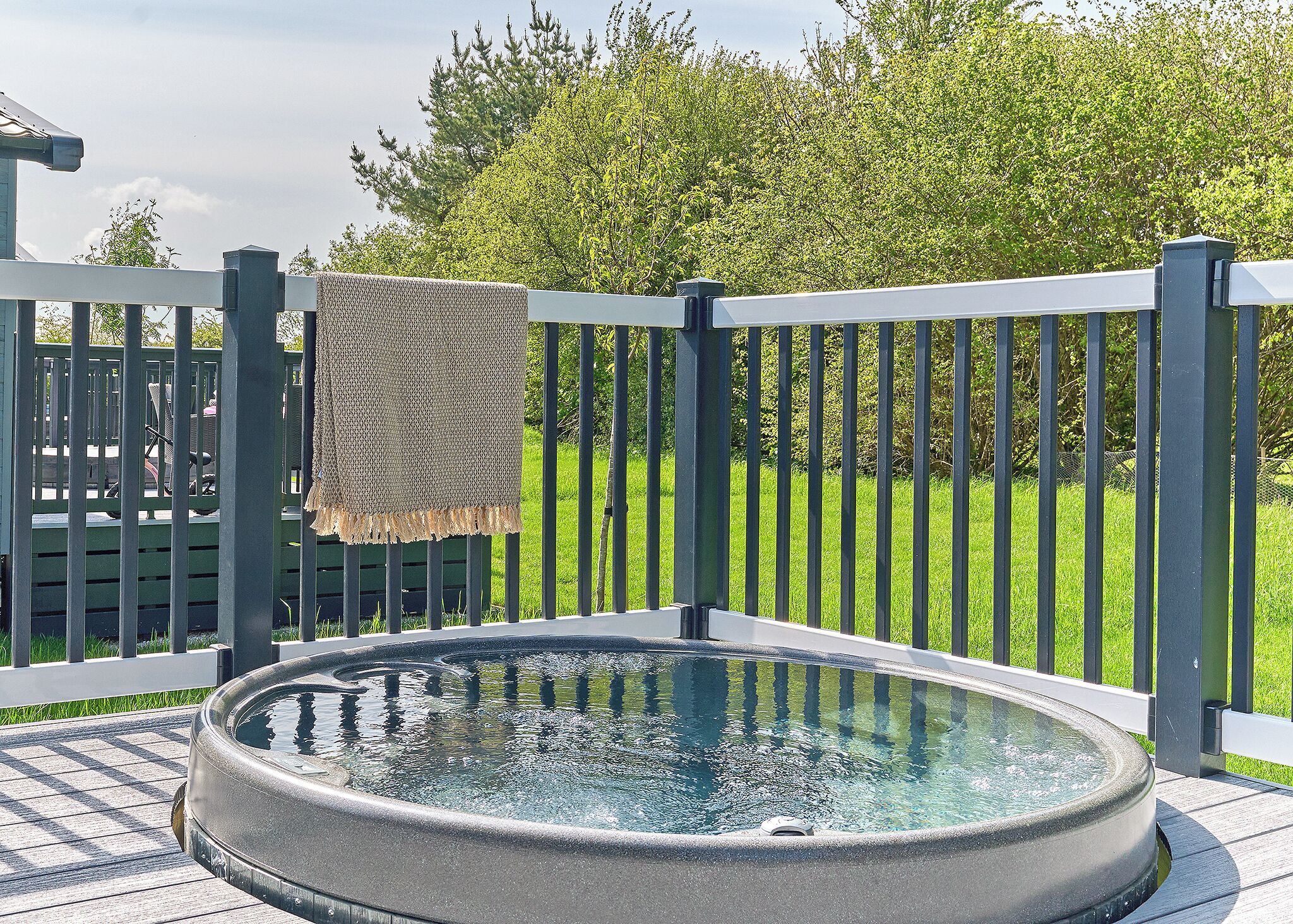 A hot tub on a wooden deck with a metal railing and a blanket hanging on it.