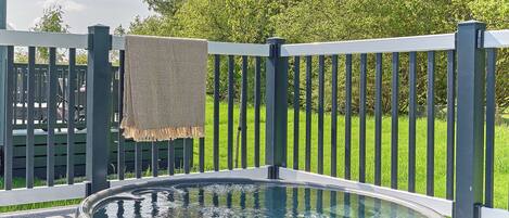A hot tub on a wooden deck with a metal railing and a blanket hanging on it.